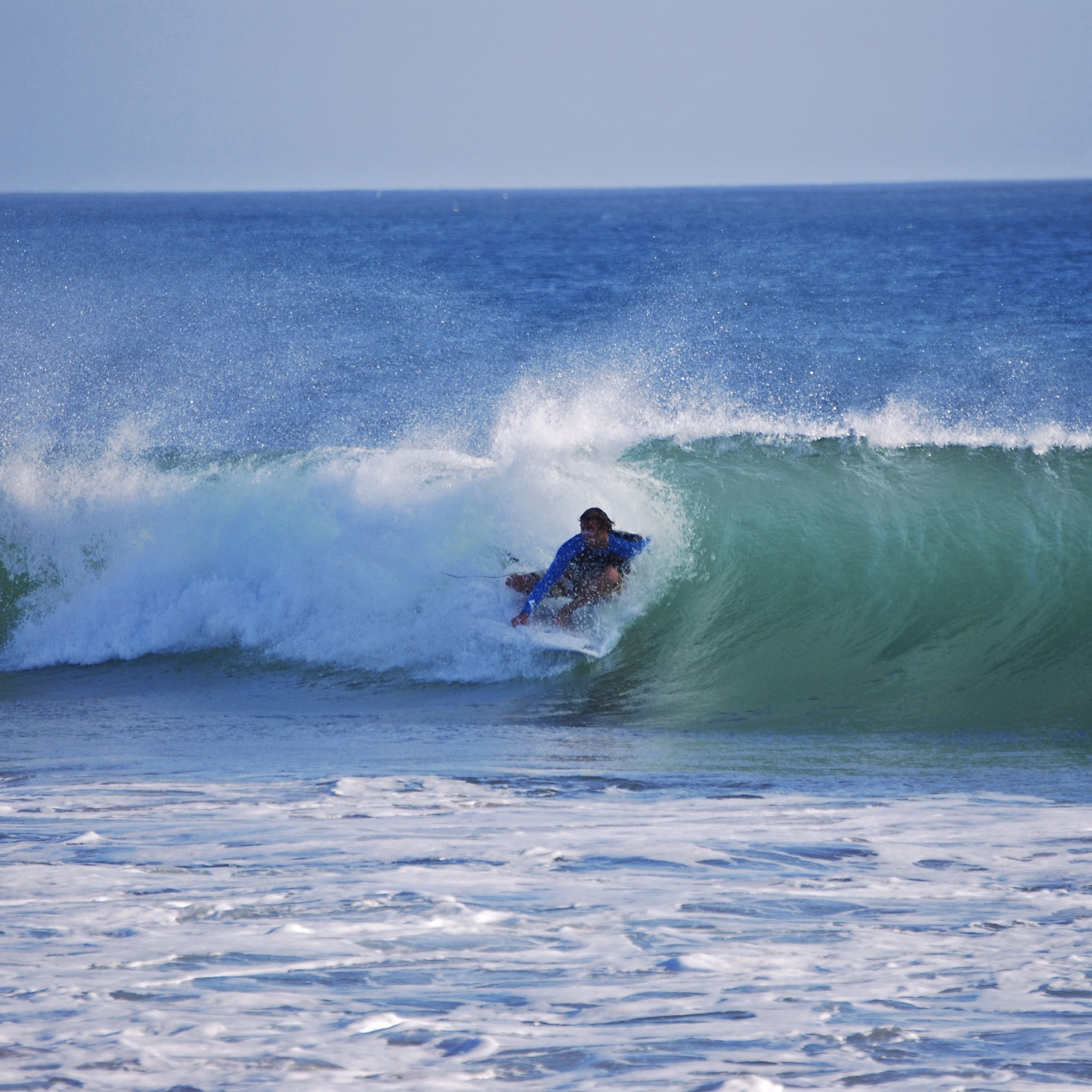Surfer in einer hohlen Welle und versucht eine Tube zu surfen. Der offshore Wind pustet den Kamm der Welle ab und Surfer scheint in der Welle zu verschmelzen.